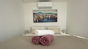 A neatly made bed with rolled towels, a painting of a cityscape, and an air conditioner on the wall. - Apartment in Okrug Gornji with Balcony, Air condition, WIFI, Dishwasher (5048-1) (Okrug Gornji)