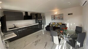 A modern kitchen with a black countertop, white cabinets, and a glass dining table with chairs. - Apartment in Okrug Gornji with Balcony, Air condition, WIFI, Dishwasher (5048-1) (Okrug Gornji)