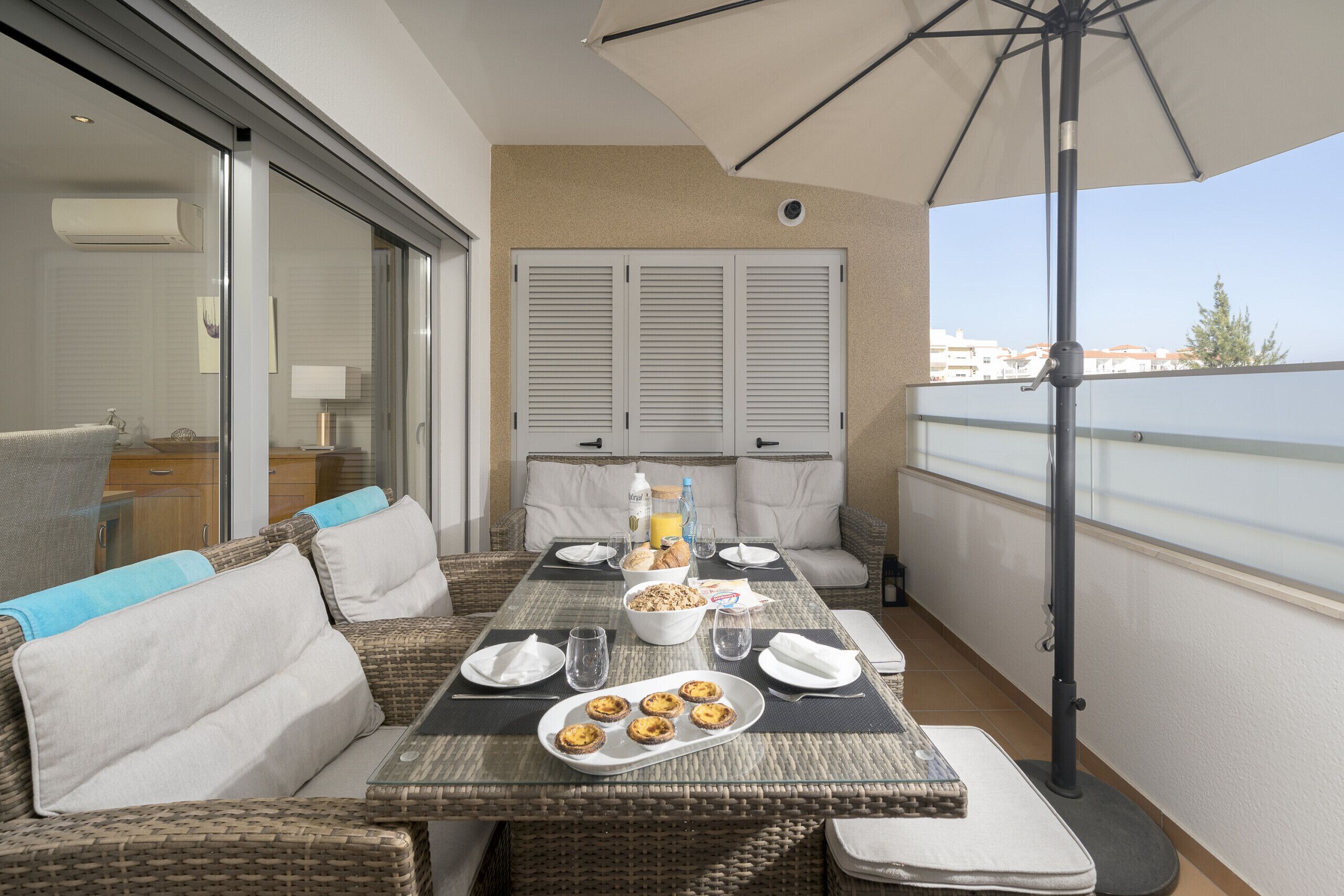 A balcony with a dining table set for breakfast, wicker furniture, and a view of the city.