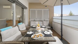 Ein Balkon mit Esstisch, gedecktem Frühstück, Korbmöbeln und Blick auf die Stadt.
