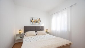 A bedroom with a large bed, two bedside tables with lamps, a headboard, a painting on the wall, and a window with curtains. - Apartment in Okrug Gornji with Seaview, Air condition, WIFI, Washing machine (5049-1) (Okrug Gornji)