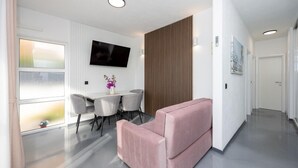 A modern living room with a flat-screen TV, a dining table with chairs, a pink sofa, and a wooden panel wall. - Apartment in Okrug Gornji with Seaview, Balcony, Air condition, WIFI (5049-2) (Okrug Gornji)
