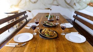 Une table à manger en bois, avec de l’assiette blanche, des couverts et des verres de vin rouge.