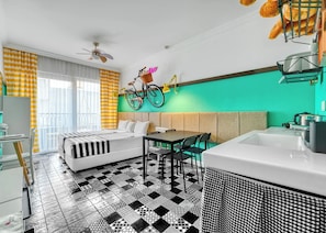 A modern hotel room with a checkered floor, a bed, a dining table with chairs, a bicycle, and a large window with curtains. - Anjeliq Downtown Hotel (Alanya)