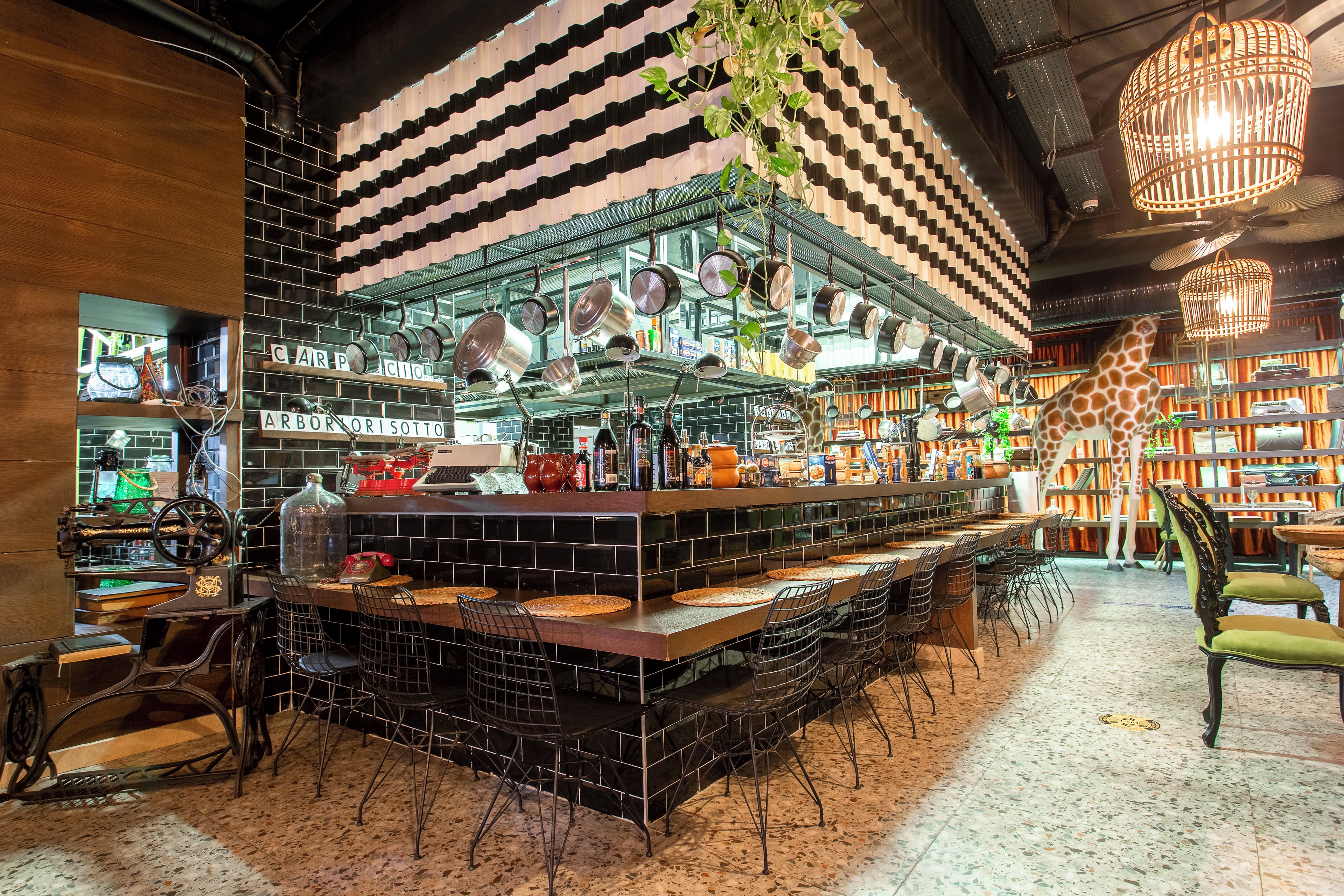 Een bar met een toonbank, hangende potten en een girafbeeld.