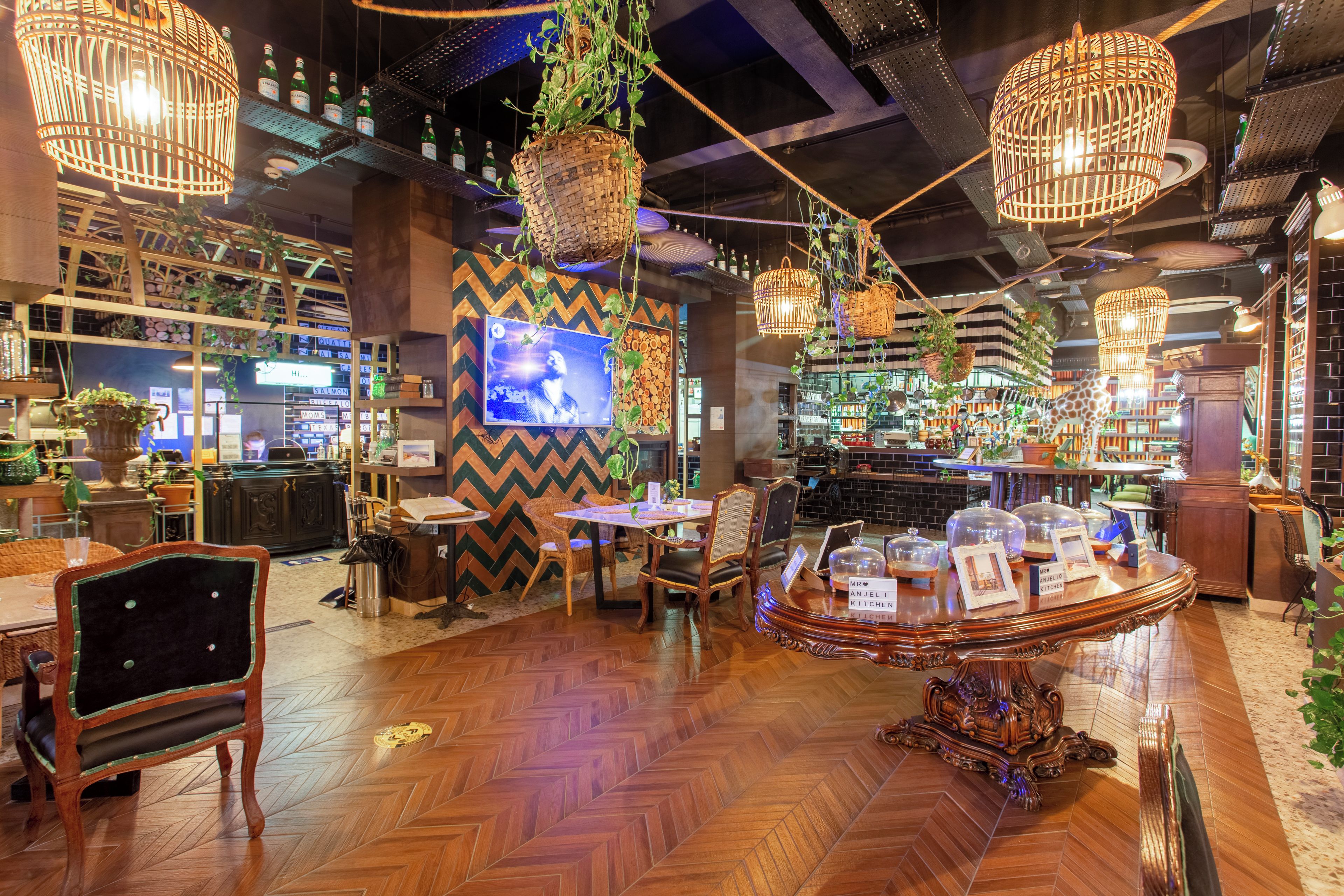 A restaurant with wooden flooring, hanging wicker baskets with plants, a television, and a bar area with shelves of bottles.