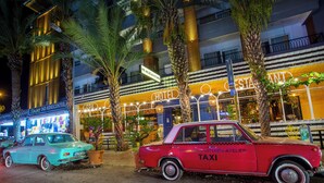 Un taxi rojo antiguo estacionado frente a un hotel con un letrero que dice 'Mr. Anjelic Kitchen Atelier' y 'Spa'.