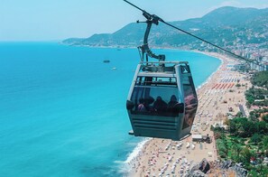 Un teleférico sobre una playa con agua azul cristalina, una orilla arenosa y un paisaje montañoso al fondo.