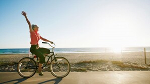 A person riding a bicycle on a paved path near a beach with the ocean in the background. - Anjeliq Downtown Hotel (Alanya)