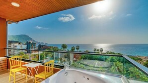 A balcony with a hot tub, yellow chairs, and a view of the sea and cityscape. - Anjeliq Downtown Hotel (Alanya)