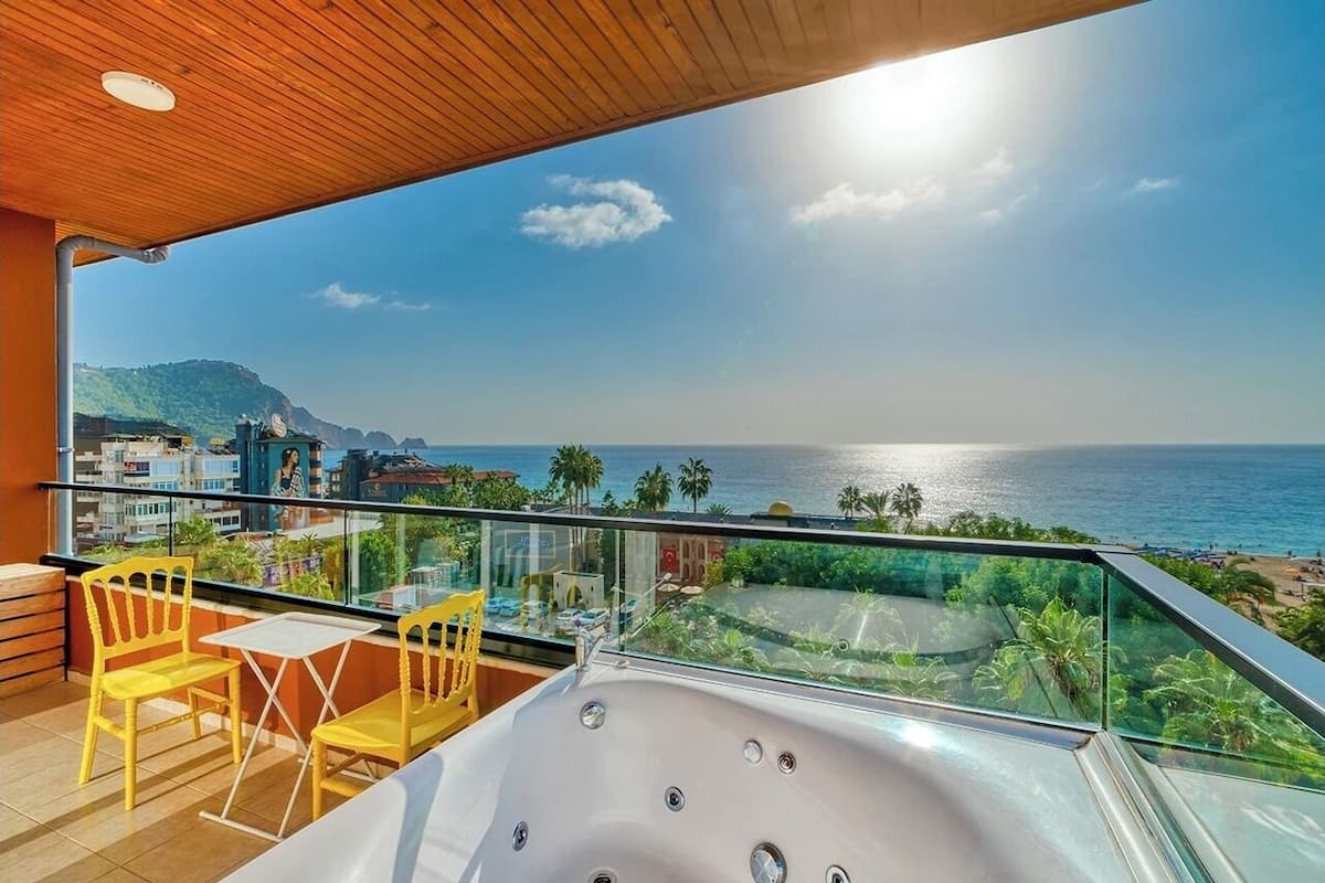 A balcony with a hot tub, yellow chairs, and a view of the sea and cityscape.