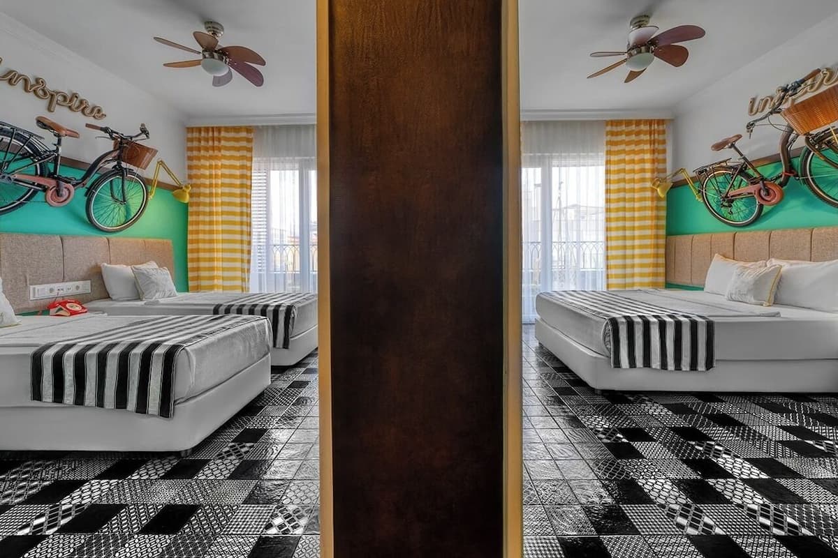 A mirrored view of a hotel room with two beds, a checkered floor, and bicycles mounted on the wall.