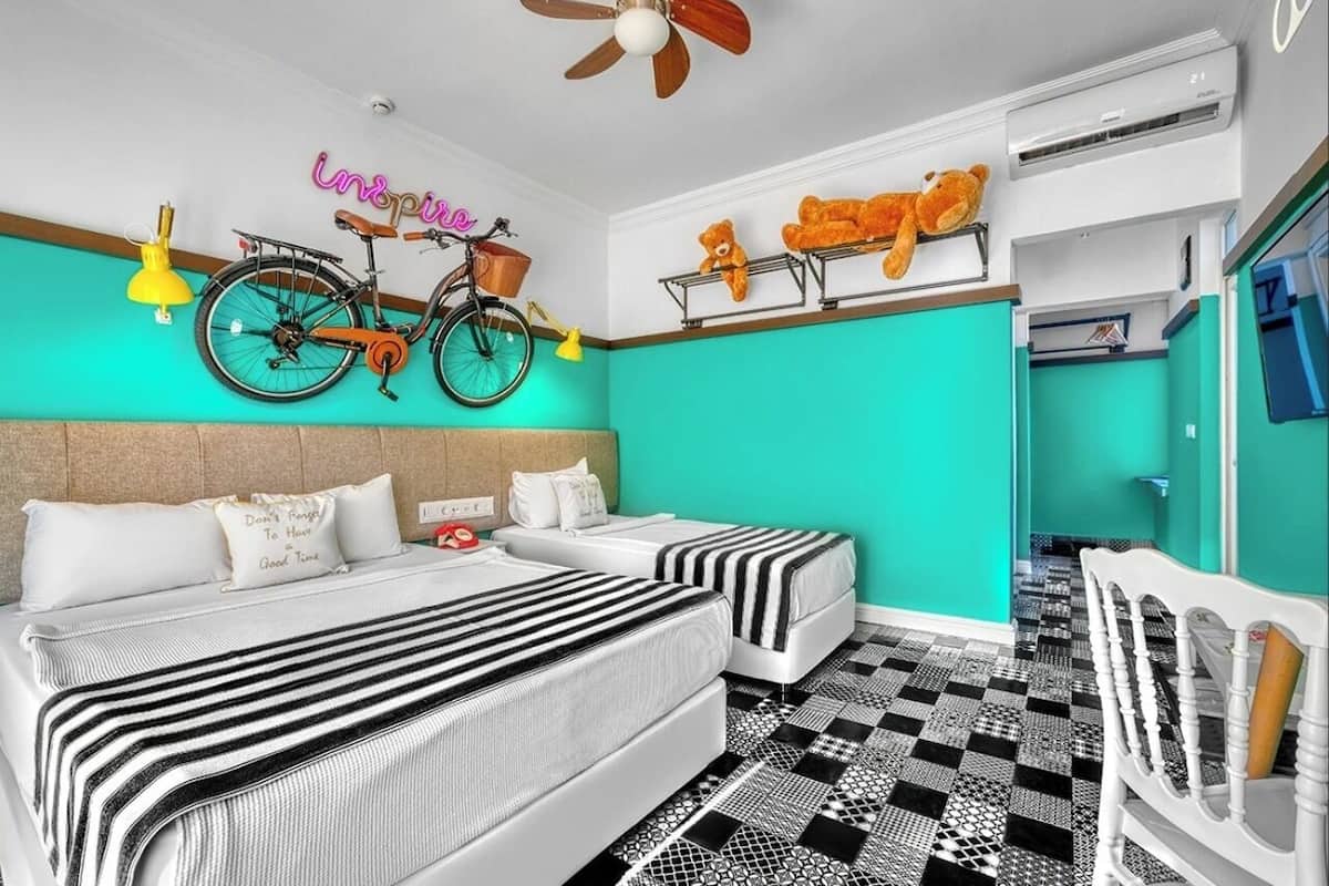 A hotel room with a teal accent wall, a bed with striped bedding, a bicycle hanging on the wall, and a ceiling fan.