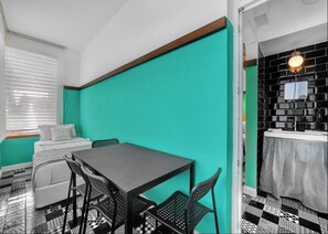 A compact room with a teal accent wall, a small dining table with four chairs, a bed with white bedding, and a black and white checkered floor. - Anjeliq Downtown Hotel (Alanya)