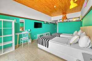 A room with two beds, a desk, a chair, a television, and a shelf with a teddy bear.