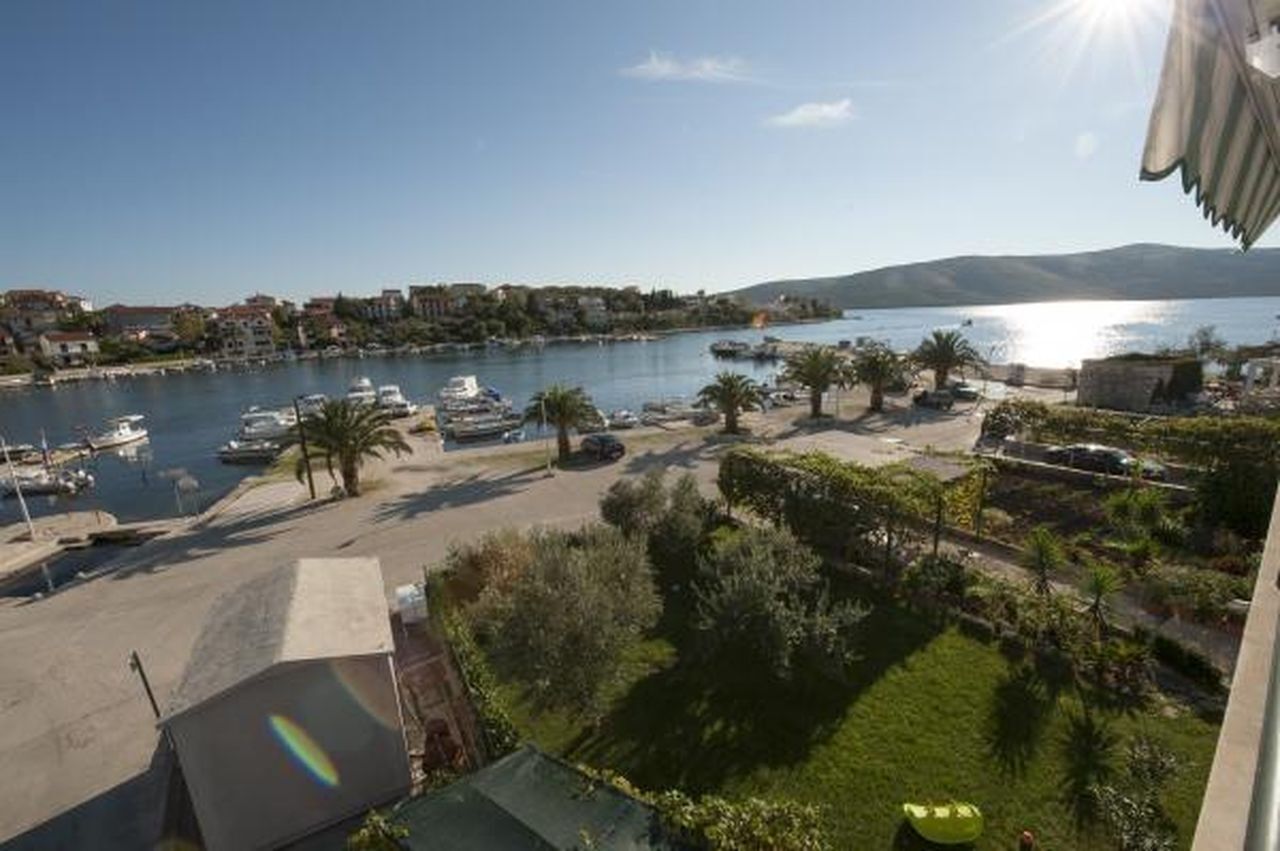 A coastal marina with boats, palm trees, and buildings along the shore.