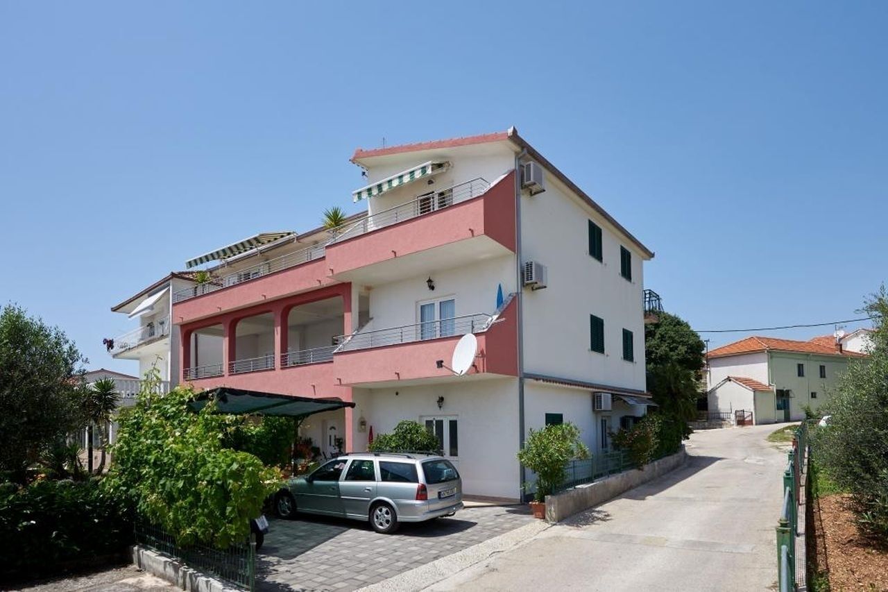 Un immeuble résidentiel à plusieurs étages, doté de balcons, d’une antenne parabolique et d’une voiture garée.