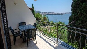 Un balcon avec une table et des chaises, donnant sur une étendue d’eau et sur de la verdure.