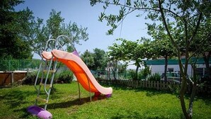 A playground with a slide and swings in a grassy area with trees and a building in the background. - Apartment in Trogir with Seaview, Balcony, Air condition, WIFI (5055-2) (Trogir)