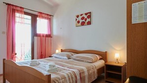 A bedroom with a wooden bed, two bedside tables with lamps, a window with pink curtains, and a wall-mounted painting. - Apartment in Trogir with Seaview, Balcony, Air condition, WIFI (5055-2) (Trogir)