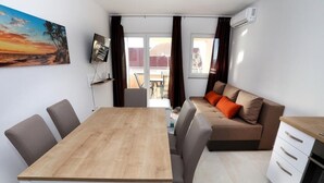 Een moderne woonkamer met een houten eettafel, grijze banken en een keuken met witte kasten.