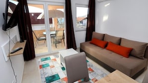 Een woonkamer met een bank, een stoel, een salontafel, een televisie en uitzicht op een balkon.