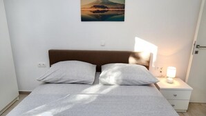 Ein ordentlich bezogenes Bett mit braunem Kopfteil, einer Nachttischlampe und einem Wandbild einer Berglandschaft.