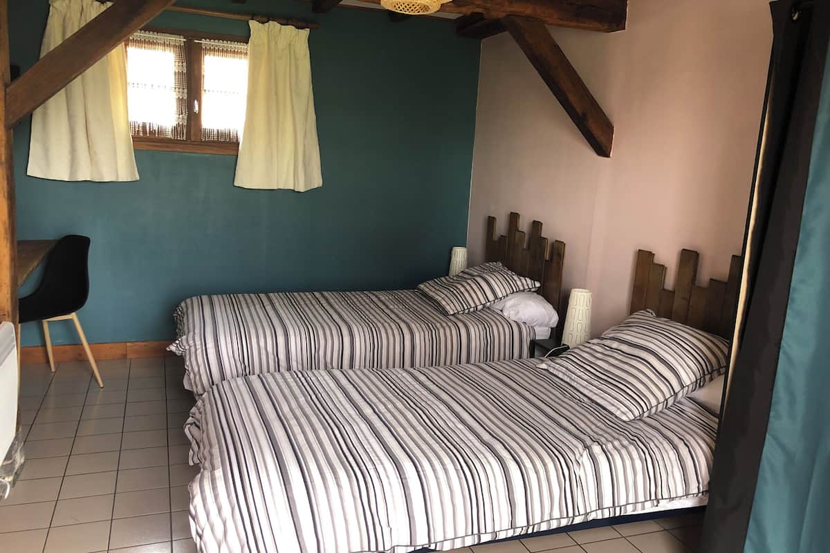 A bedroom with two beds, a chair, and a window with curtains.