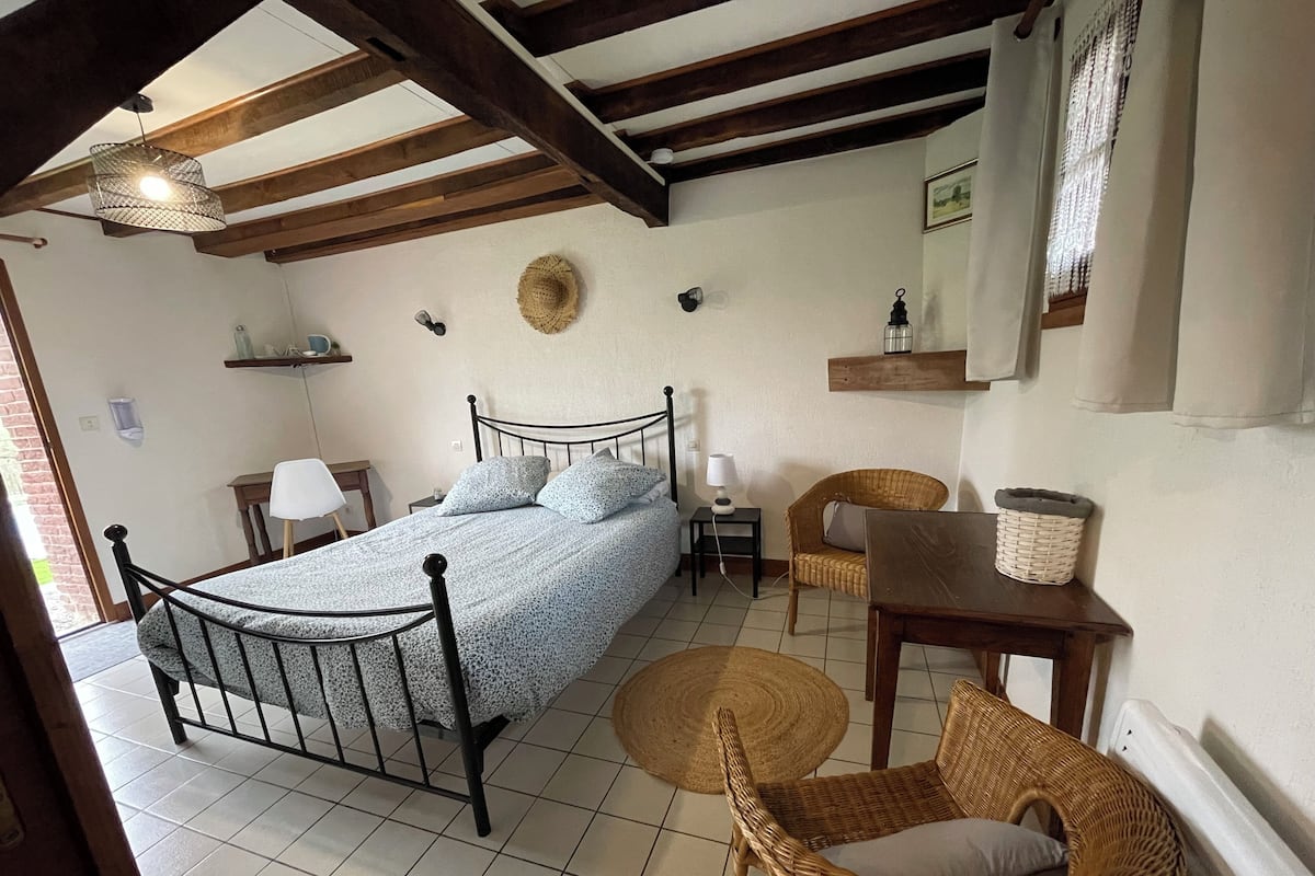 A bedroom with a bed, a chair, a table, a lamp, and a hanging light fixture.