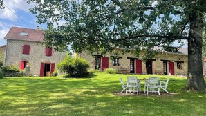 A stone building with red shutters, a lawn, and outdoor seating. - Maison d'hôtes Ourdeaux et gîte Chez Rouchon (Alleyrat)
