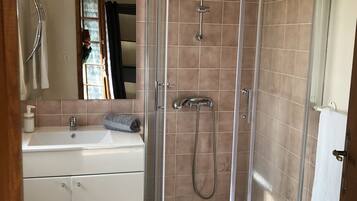 Un baño con ducha de vidrio, lavamanos y espejo.