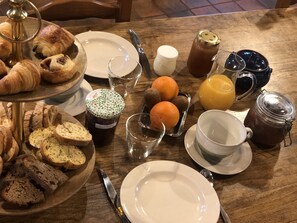 A breakfast setting with croissants, bread, oranges, and various beverages on a wooden table. - Maison d'hôtes Ourdeaux et gîte Chez Rouchon (Alleyrat)