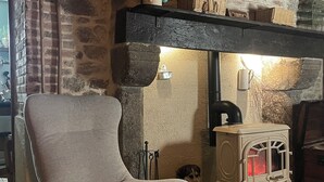 A cozy room with a stone wall, a wooden chair, a vintage stove, and a basket on the shelf. - Maison d'hôtes Ourdeaux et gîte Chez Rouchon (Alleyrat)