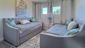 A bedroom with a grey sofa bed, a smaller bed, a ceiling fan, a window with curtains, and a painting of an owl. - 3 Bedroom Cottage at Delaronde Resort (Big River)