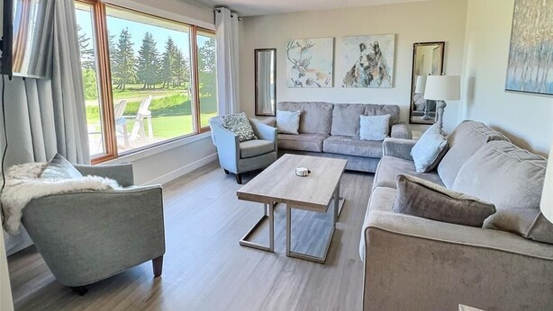 A spacious living room with a large window, a sofa set, a coffee table, and artwork on the walls. - 3 Bedroom Cottage at Delaronde Resort (Big River)