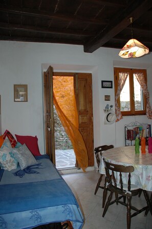 A room with a bed, a dining table with chairs, a window with curtains, and a door leading outside.