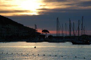 A marina with boats docked, a sunset in the background, and buildings along the waterfront.