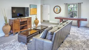 Una sala de estar con sofá, mesa de centro, televisor, aparador de madera y mesa de billar.