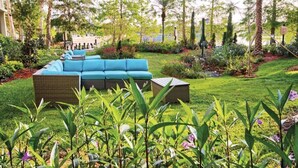 Un jardín exuberante con un sofá azul y una pequeña mesa, rodeado de diversas plantas y árboles.