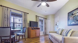 Una sala de estar con piso de madera, un sofá, un televisor sobre un mueble de madera y dos sillones.