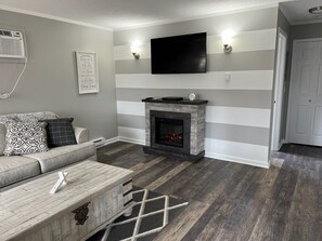 Uma sala de estar com lareira, sofá, mesa de centro e uma televisão de tela plana na parede.