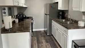 A modern kitchen with white cabinets, a stainless steel refrigerator, a granite countertop, and a sink. - Adventure Acres- Suite C5 (Holly)