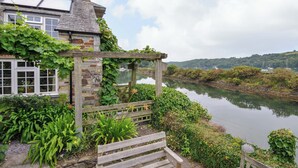 A riverside property with a wooden pergola, a bench, and lush greenery. - Island House (Fowey)