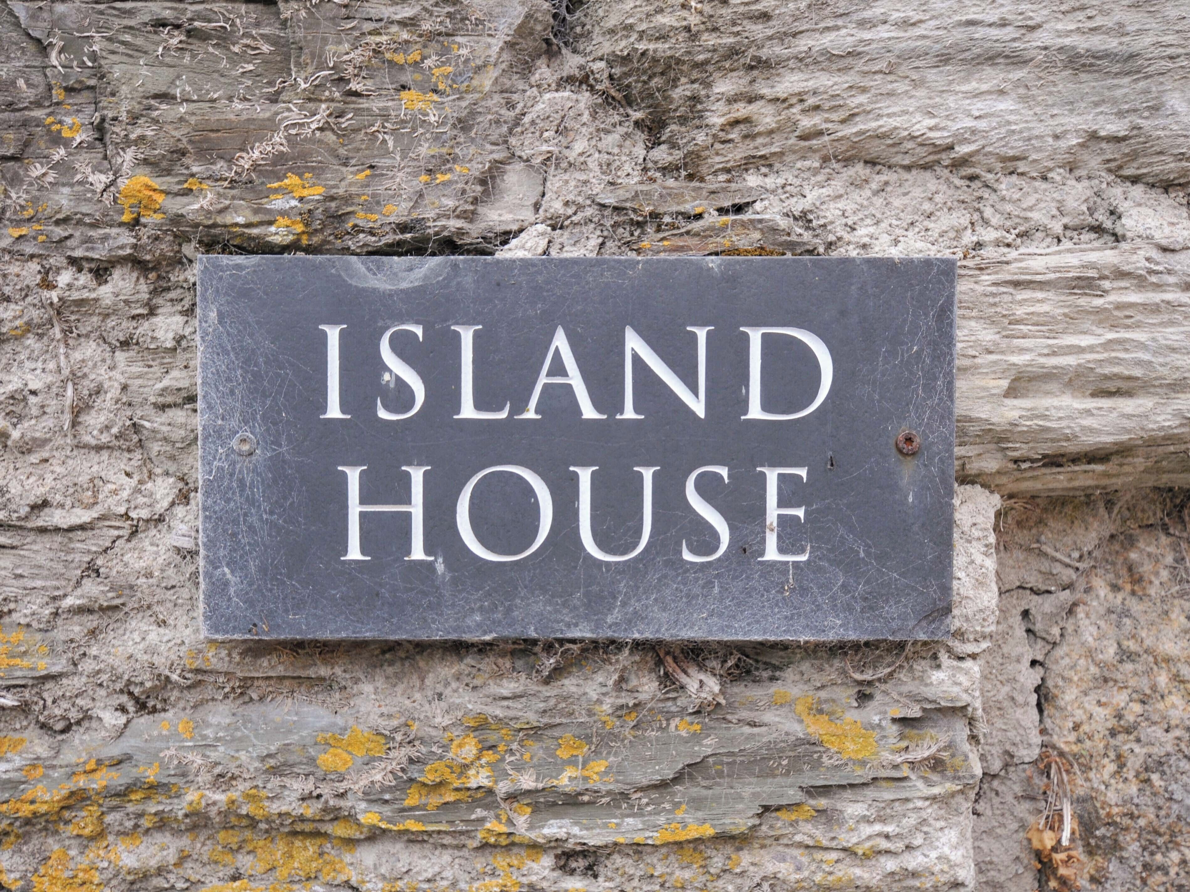 A stone sign with the text "ISLAND HOUSE" against a textured stone wall.