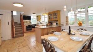 A spacious kitchen with a central island, wooden cabinets, and a dining area with a large table set for four. - Island House (Fowey)