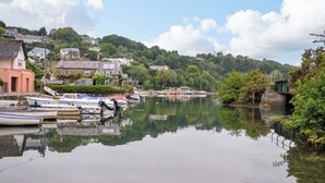 A calm river with boats docked on the left, surrounded by houses and greenery. - Island House (Fowey)