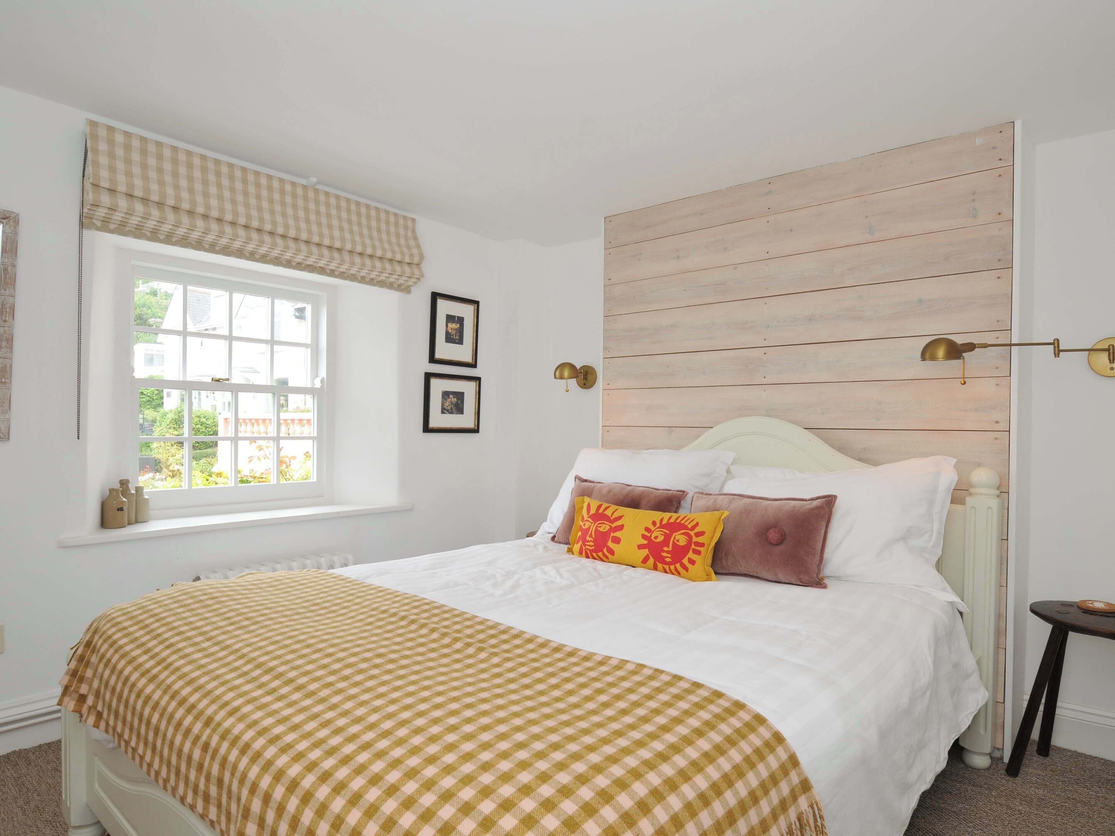 Un dormitorio con un ventanal grande, una cama con colcha de cuadros y un cabecero de madera.