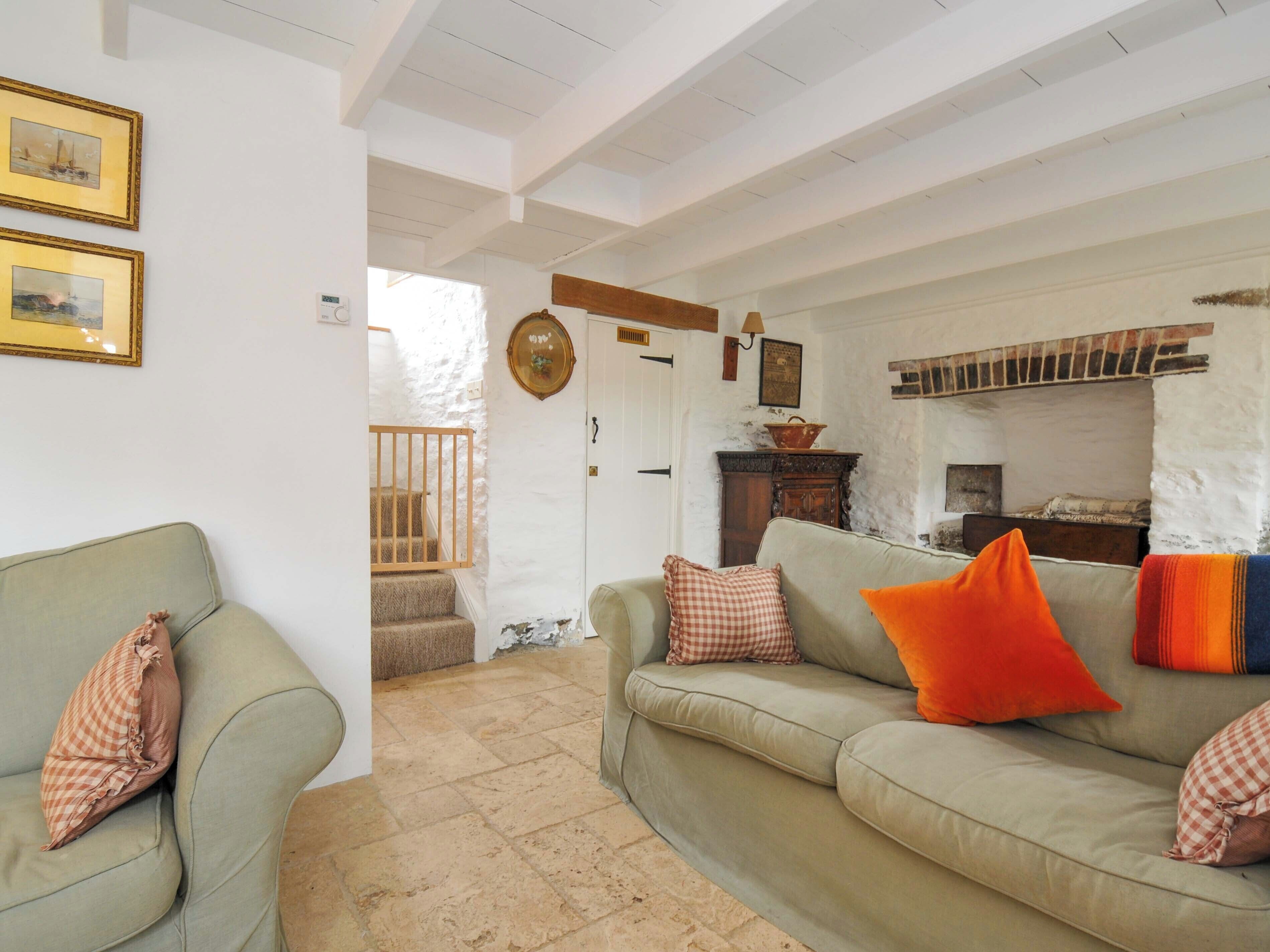 Ein gemütliches Wohnzimmer mit einer Couch, einem karierten Kissen und einem leuchtend orangefarbenen Kissen. Eine Holztreppe führt in einen anderen Raum.
