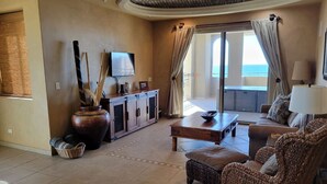A spacious living room with a large window, a flat-screen TV, a wooden cabinet, wicker furniture, and a large vase.