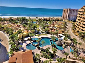 Un resort con varias piscinas, palmeras y vistas a la playa.